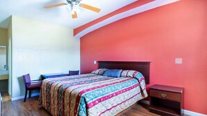 Ein Schlafzimmer mit Bett, Schreibtisch, Stuhl, Nachttisch und Deckenventilator.