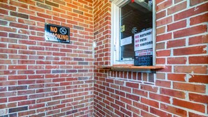 Eine Ecke eines Backsteingebäudes mit einem 'RAUCHVERBOT'-Schild und einem Fenster mit der Aufschrift 'KEINE RÜCKERSTATTUNGEN, KEINE HAUSTIERE, KEINE BESUCHER'.