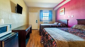 Ein Hotelzimmer mit Bett, Schreibtisch, Mikrowelle, Fernseher und einem Fenster mit Vorhängen.