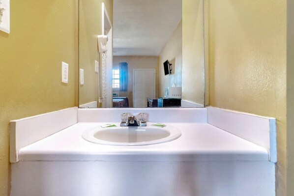 A bathroom with a white sink, mirror, and a view of a hallway with a door and a window.