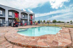 Un hotel con piscina, area salotto esterna e parcheggio recintato.