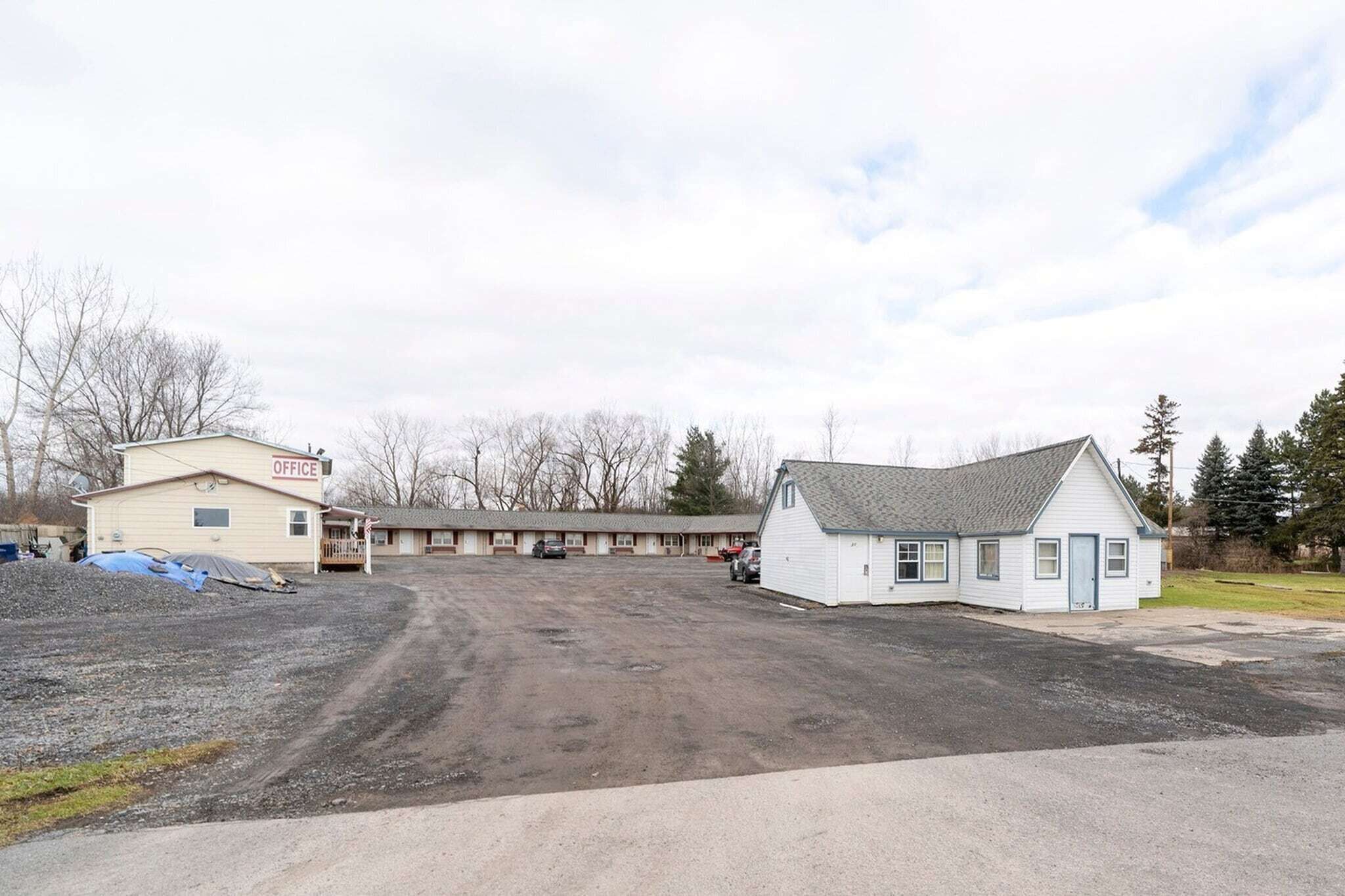 A motel with a large parking lot, a small office building labeled 'OFFICE,' and a single-story building with a sloped roof.