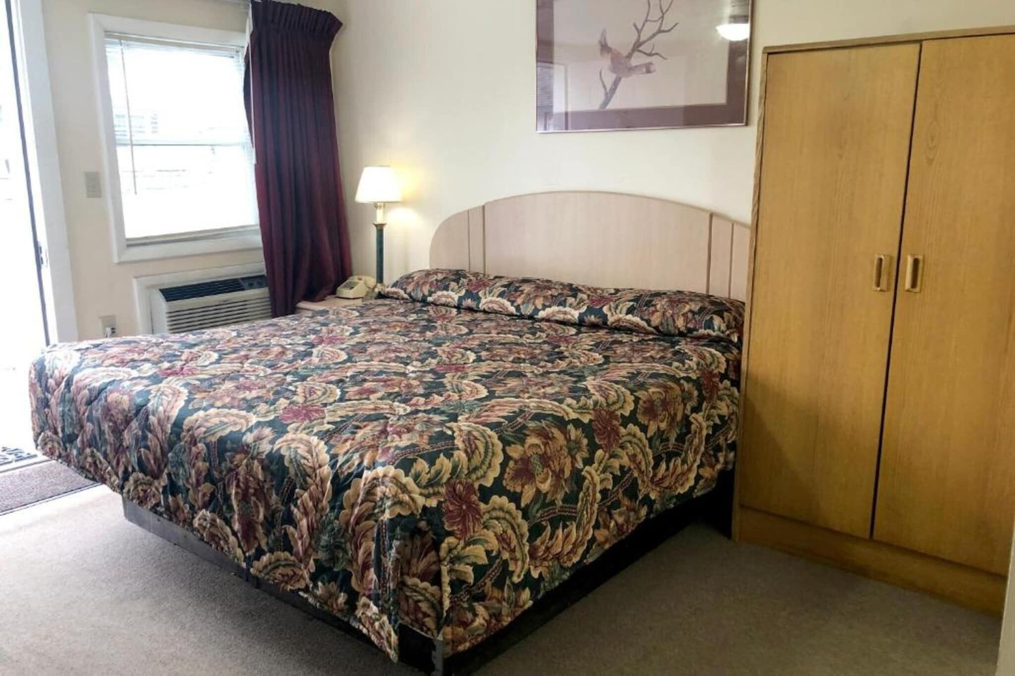 A bedroom with a bed, a nightstand, a lamp, a wardrobe, and a window with curtains.