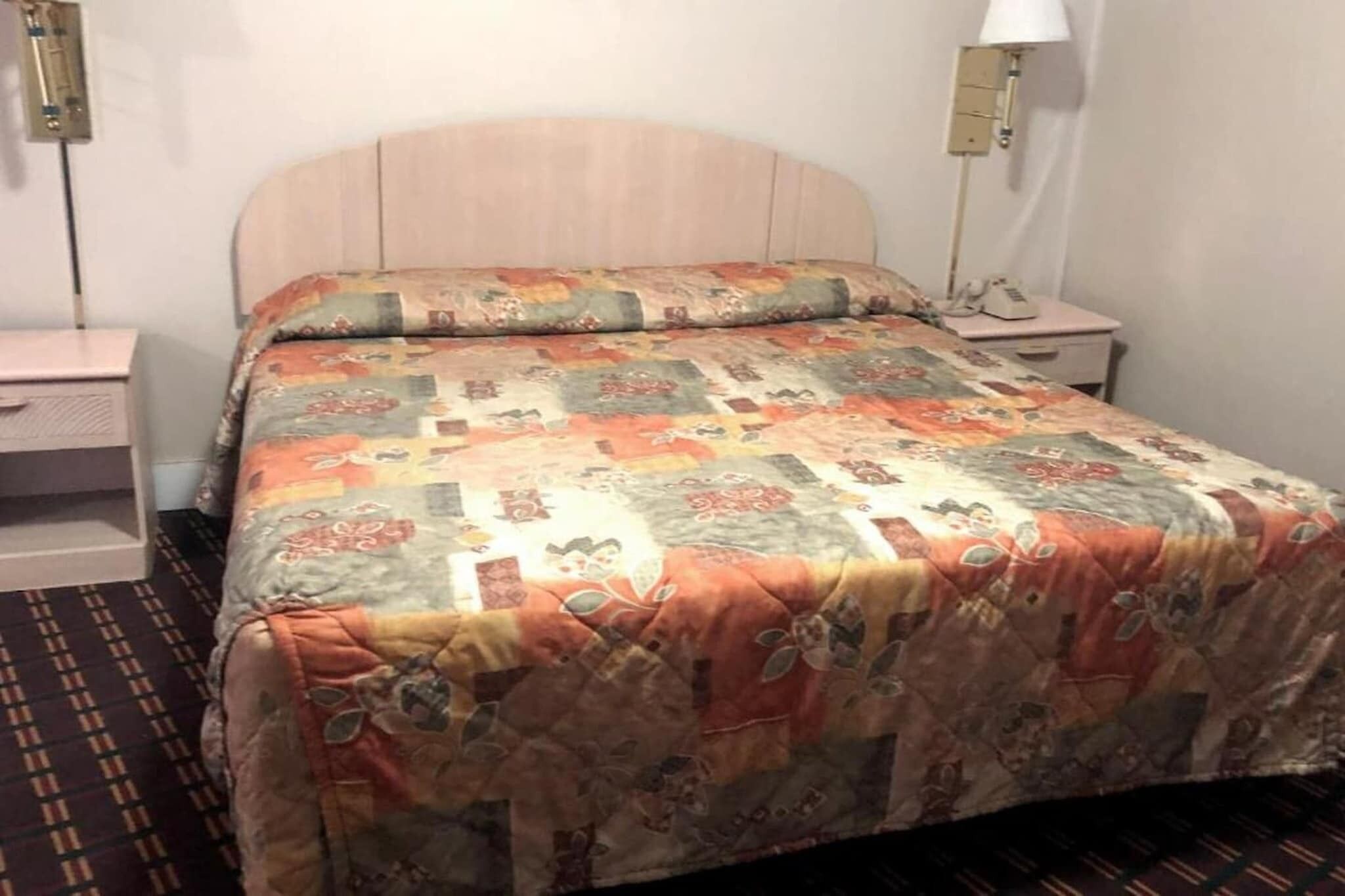A bed with a quilt, a bedside table, a lamp, and a wall socket.