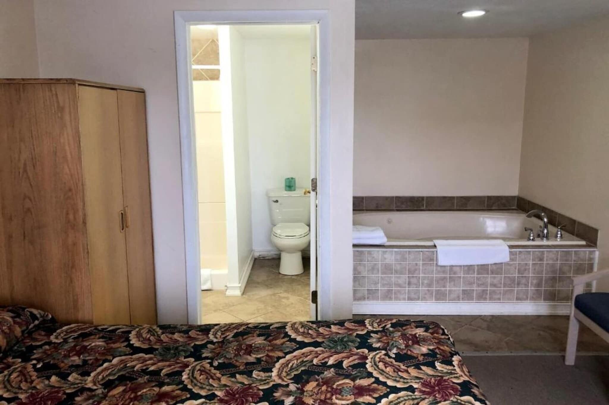 Ein Schlafzimmer mit einem Bett, einem Holzschrank und einem Badezimmer mit Badewanne und Toilette.