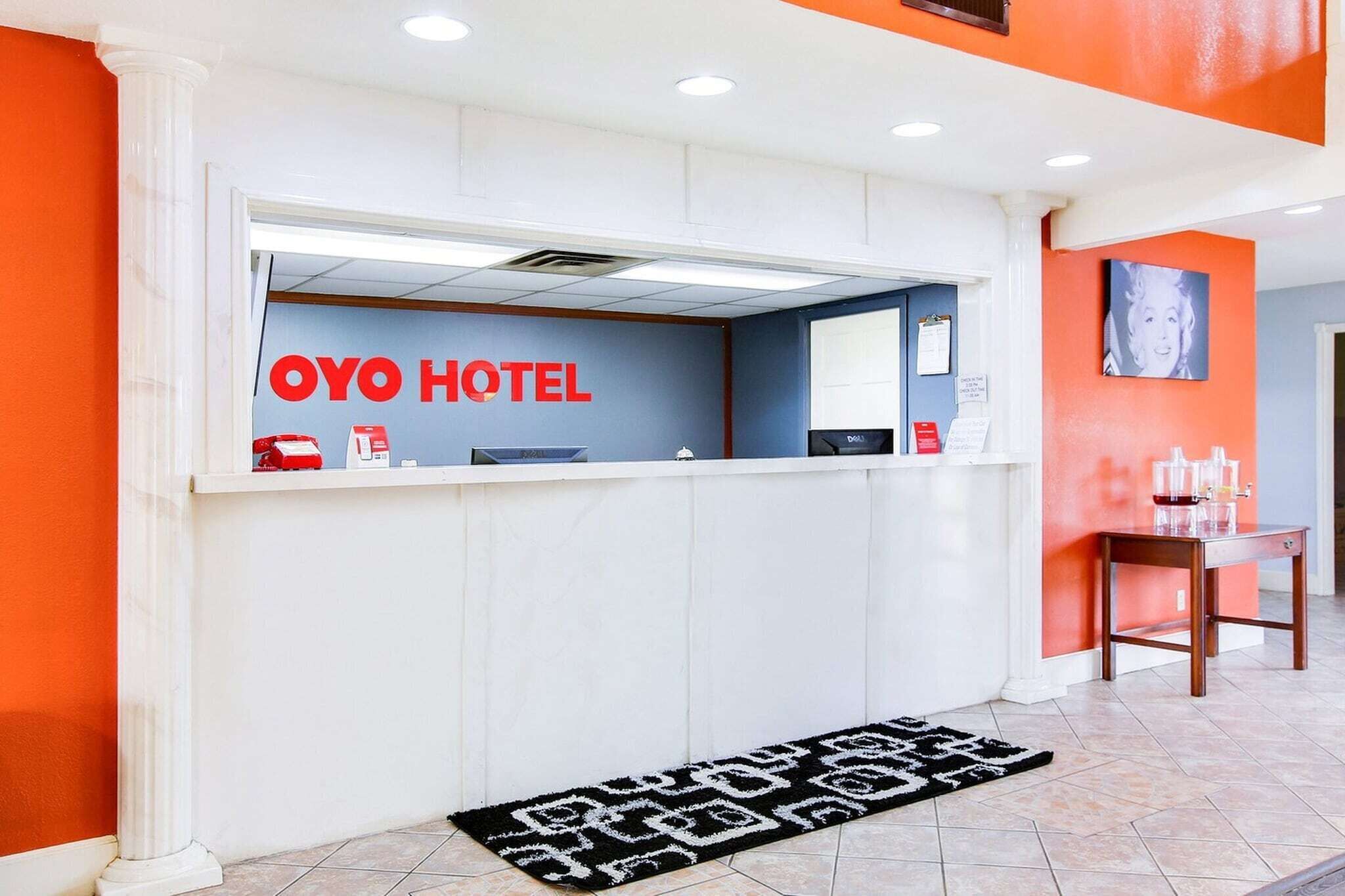 Una reception con la segnaletica 'OYO HOTEL', un banco della reception, un piccolo tavolo con una sedia e un tappeto decorato.