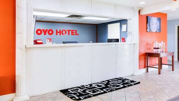 Una reception con la segnaletica 'OYO HOTEL', un banco della reception, un piccolo tavolo con una sedia e un tappeto decorato.