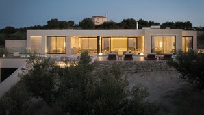 Ein modernes Haus mit großen Glasfenstern, einem Swimmingpool und Sitzgelegenheiten im Freien.