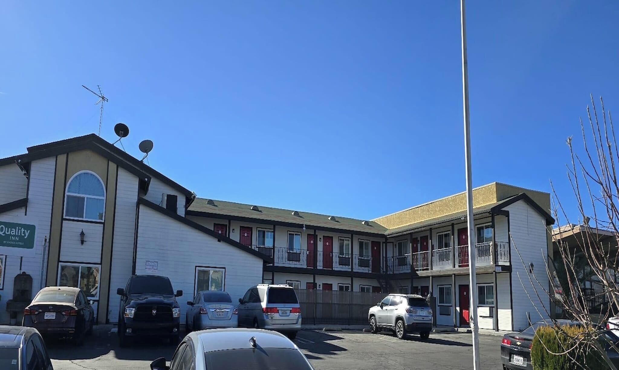 A motel with multiple rooms, a parking lot, and a clear blue sky.