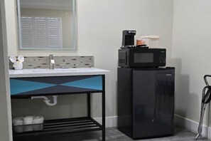 Una kitchenette compacta con microondas, cafetera y un refrigerador pequeño.