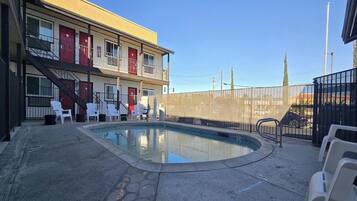 A pool area with white chairs, a building with red doors, and a fence.