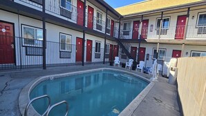 A pool area with a clear blue pool, a set of stairs leading to a balcony, and a row of white chairs. - King Bed|Walkin|Victorville (Victorville CA)