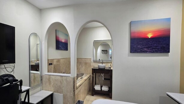 A modern bathroom with a bathtub, a sink, and a mirror. There are two arched doorways leading to other rooms.