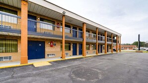 A multi-story motel with a flat roof, multiple balconies, and a parking lot.