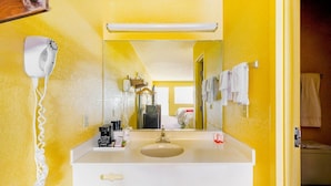 A bathroom with a yellow wall, a white sink, a mirror, a hairdryer, and a towel rack.