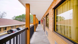 A corridor with a covered walkway, brick walls, and windows with blinds.