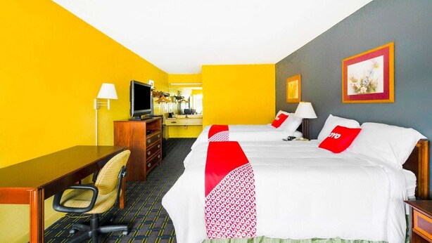 A hotel room with a bed, desk, chair, television, and a mirror.
