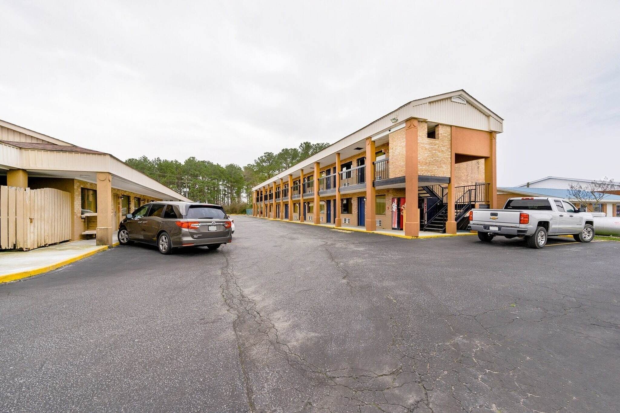 Un motel avec un couloir central, des chambres individuelles de chaque côté et un parking où l’on peut garer deux voitures.