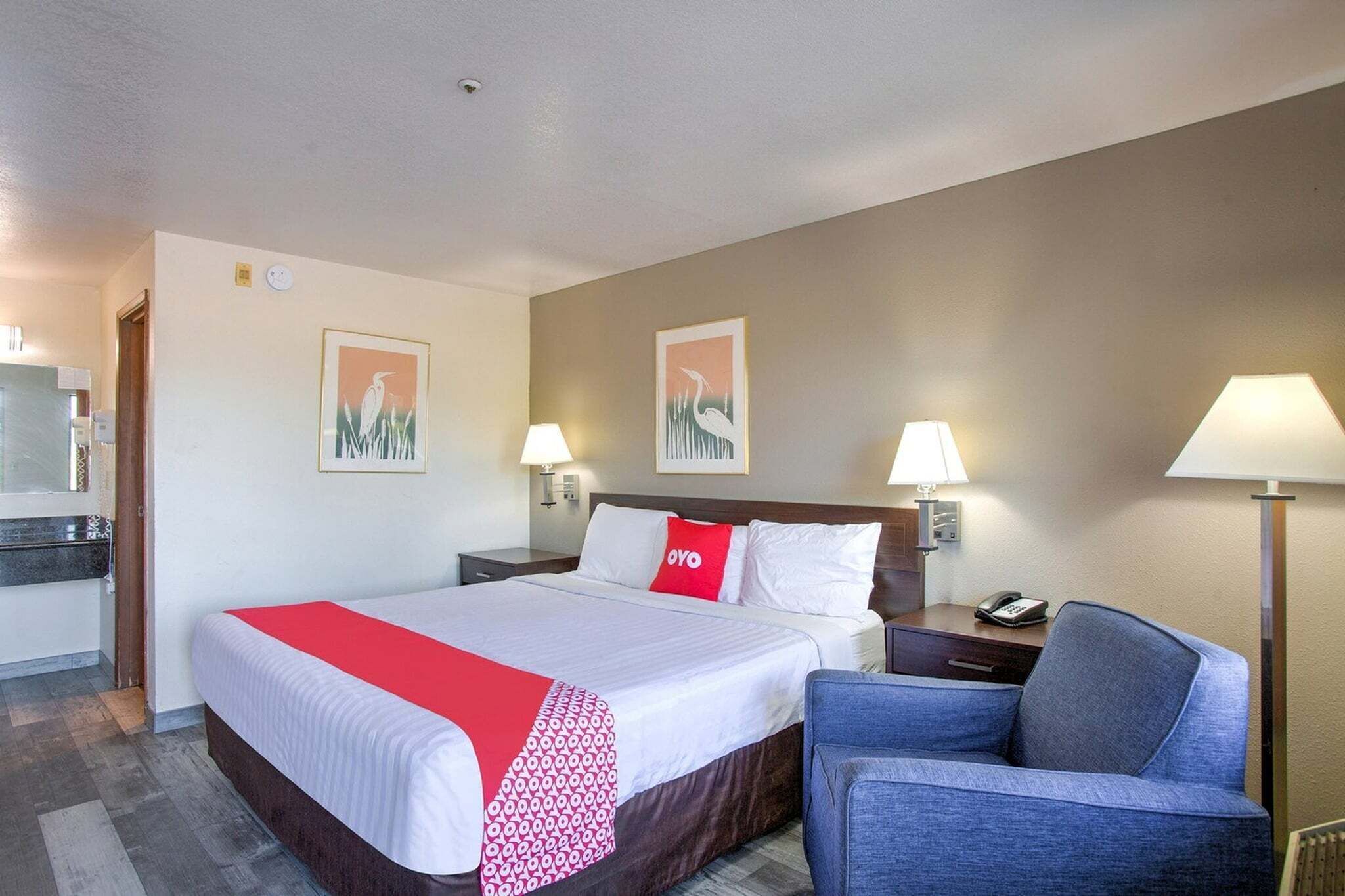 Een hotelkamer met een bed, een stoel, een bureau met een lamp en kunstwerken aan de muur.