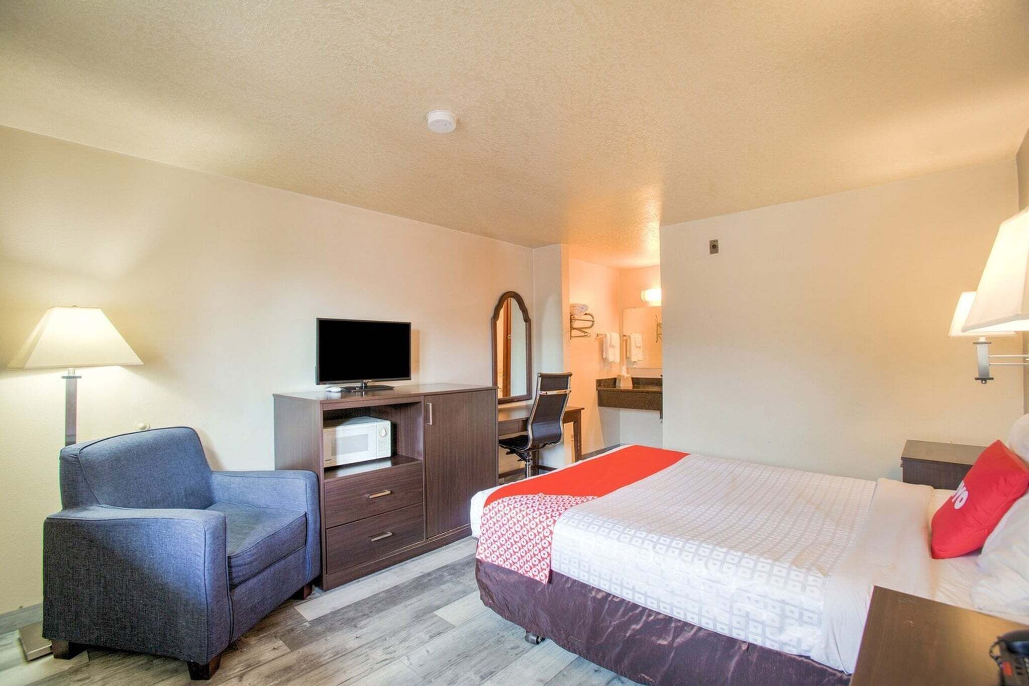 A hotel room with a bed, a desk with a computer, a chair, a TV, and a microwave.