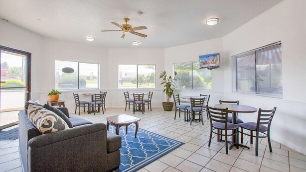 A spacious room with a ceiling fan, multiple windows, a television, and a dining area with chairs and tables.