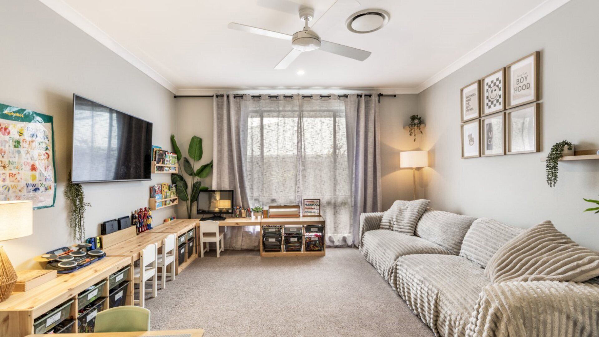 Un salon confortable avec un ventilateur de plafond, un téléviseur, une bibliothèque, un bureau, un canapé et une fenêtre avec des rideaux.
