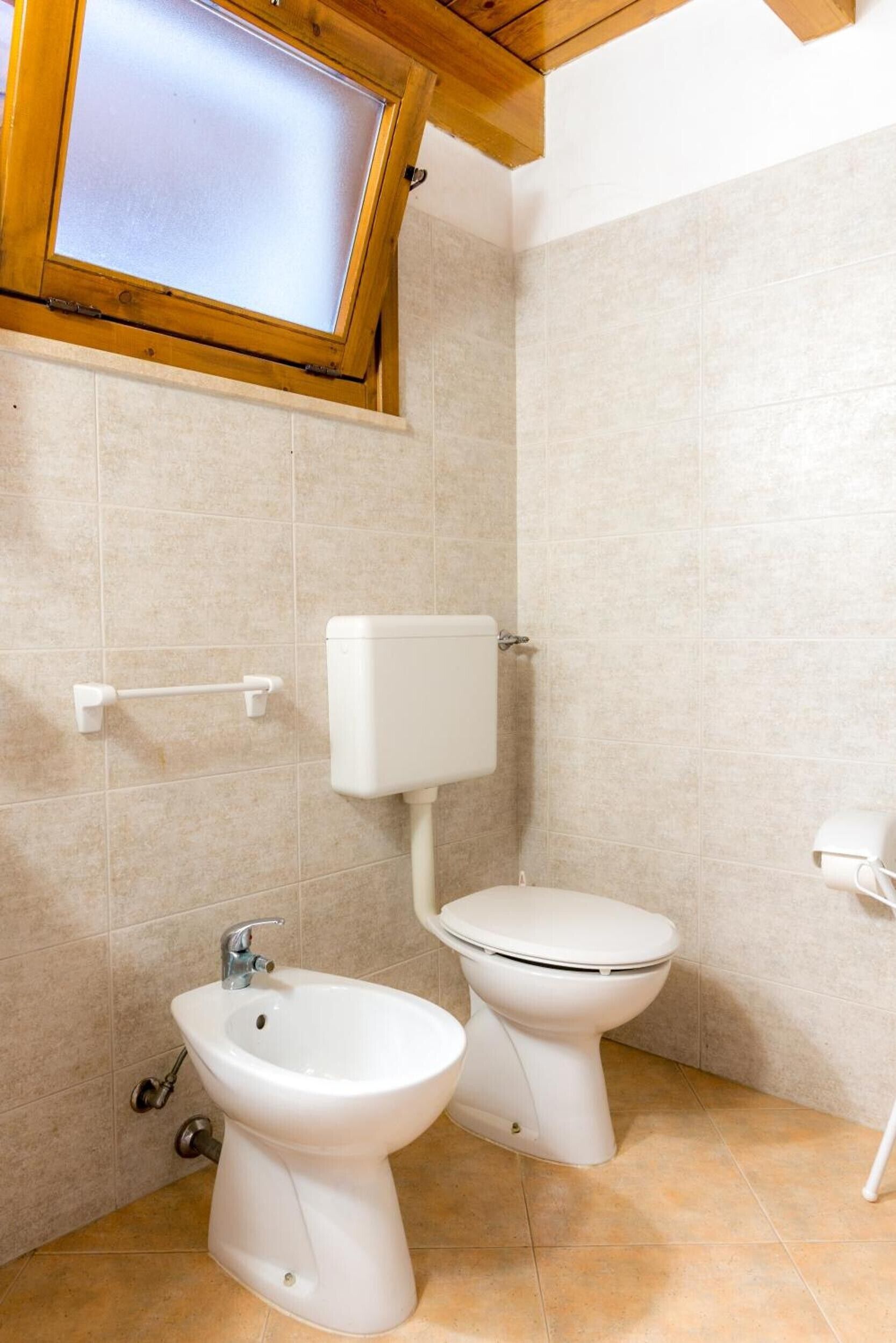 Ein Badezimmer mit Toilette, Bidet und einem Fenster über der Toilette.