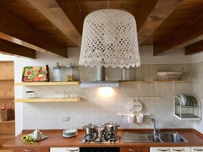 Cocina con vigas de madera, una lámpara colgante de encaje blanco, electrodomésticos de acero inoxidable y un salpicadero de azulejos.