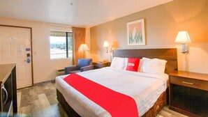 A hotel room with a bed, bedside lamps, a desk, a chair, a window with curtains, and a door.