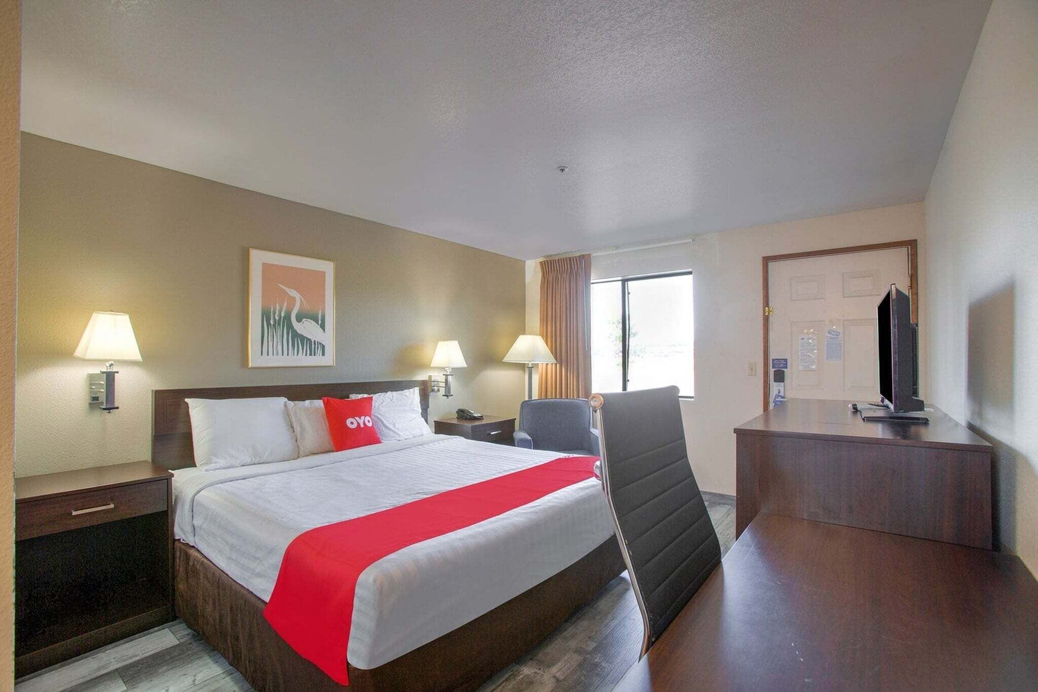 A hotel room with a bed, bedside lamps, a desk with a TV, and a window with curtains.