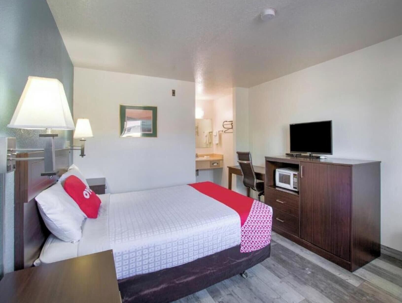 Ein Hotelzimmer mit Bett, Nachttischlampen, Fernseher, Schreibtisch und einer Mikrowelle.