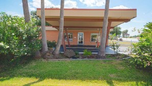 A building with a covered entrance, surrounded by trees and a grassy area. - Weslaco TX|King Bed Smoking (Weslaco TX)