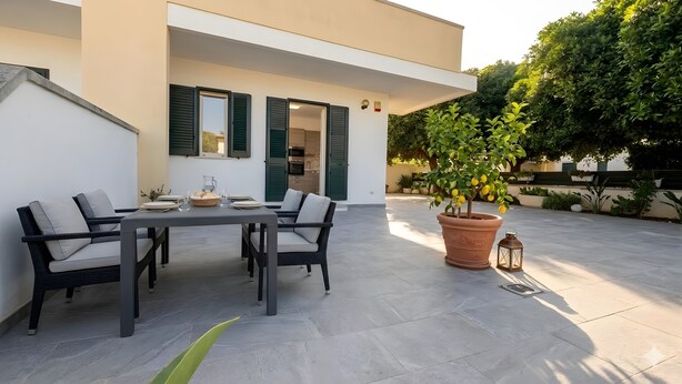 A patio with a table and chairs, a potted plant, and a lantern.