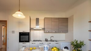 A modern kitchen with white cabinets, a built-in oven, a stove, a sink, and a washing machine.