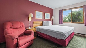 A hotel room with a bed, a red armchair, two bedside lamps, and a window with curtains.