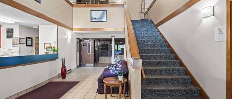 A hotel lobby with a reception desk, a staircase, and a sofa.