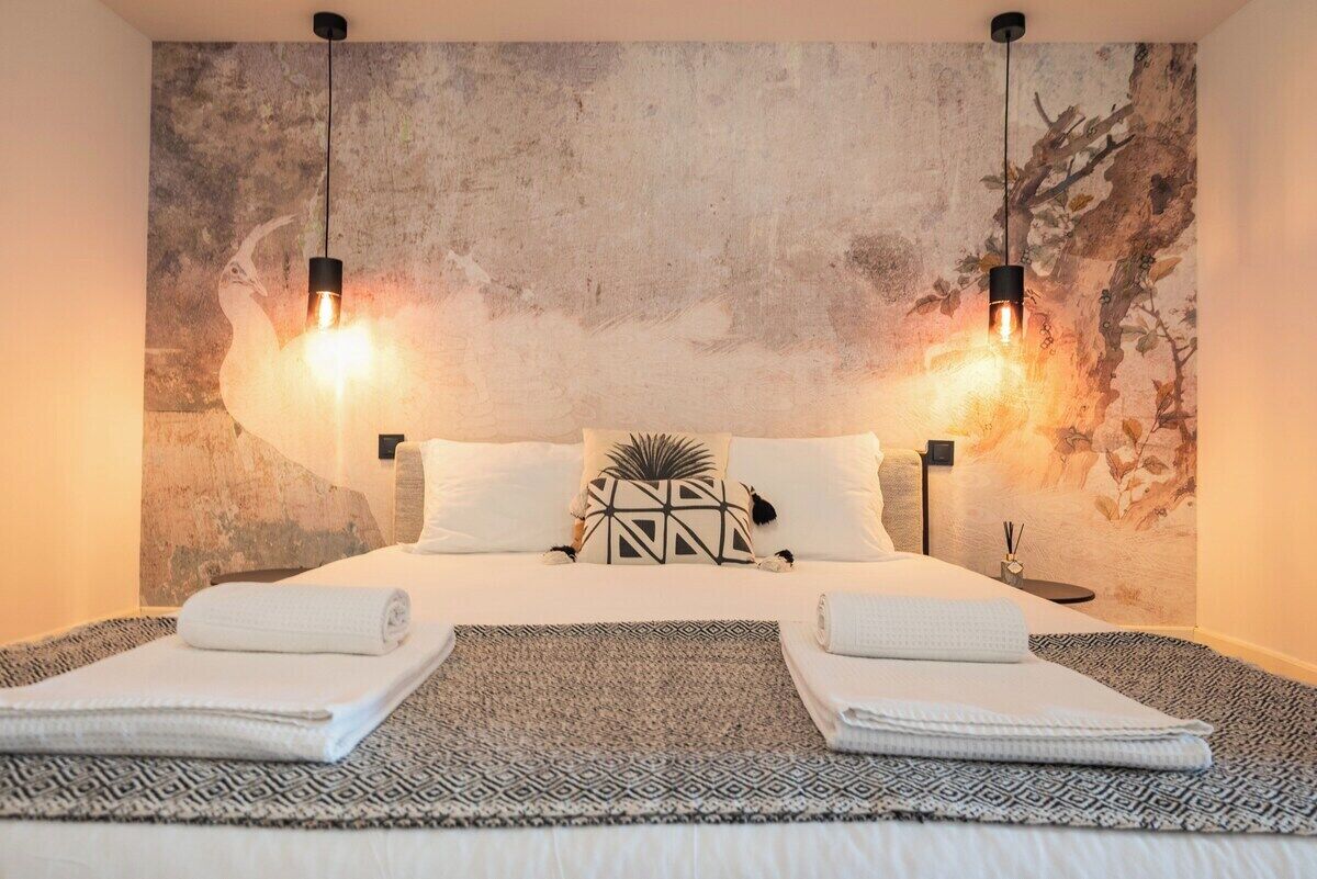 A hotel room with a large bed, two bedside lamps, a textured wall mural, and a small side table with a candle.