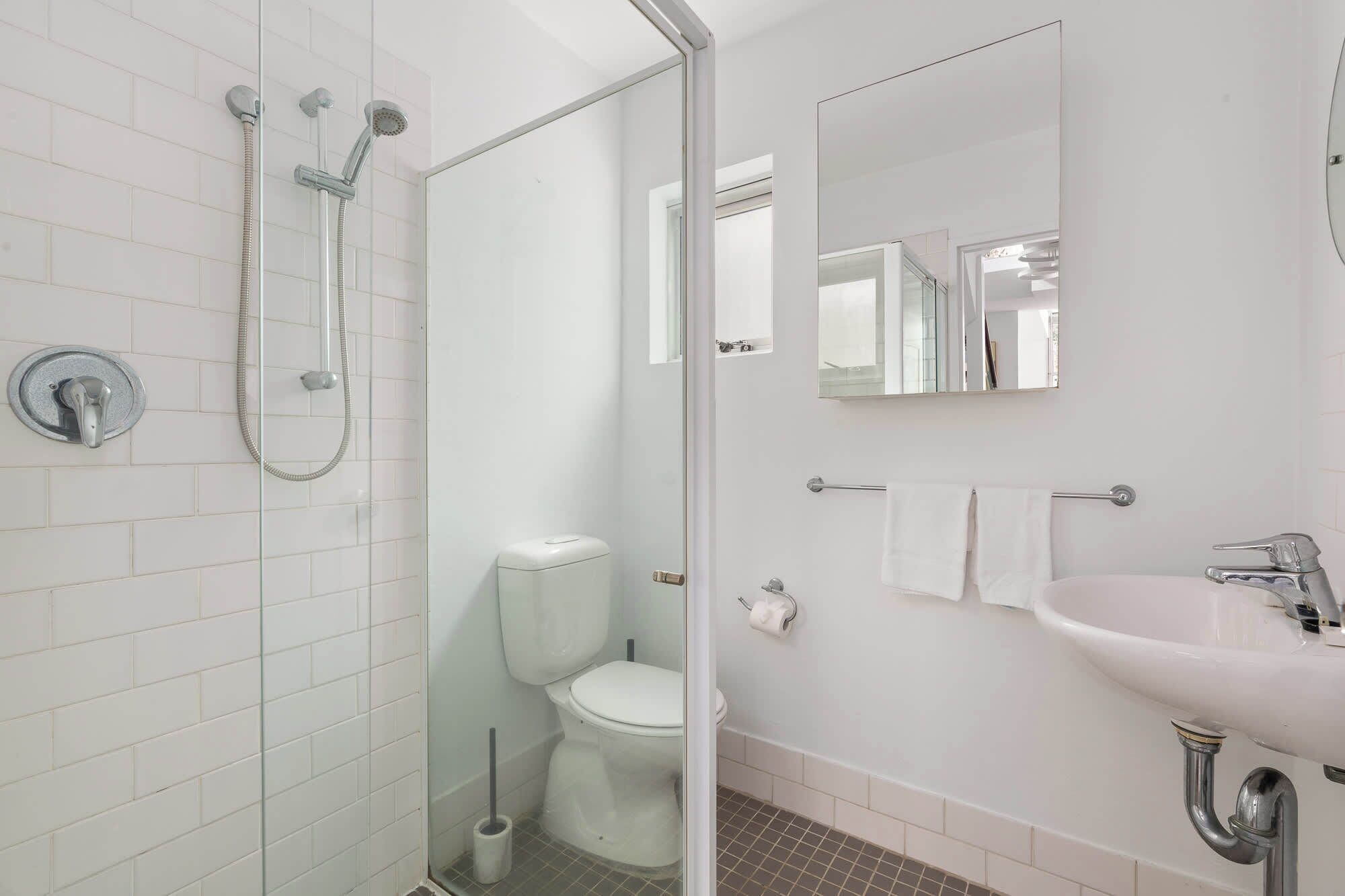 Een moderne badkamer met een glazen douchecabine, toilet, wastafel met spiegel en een handdoekrek.