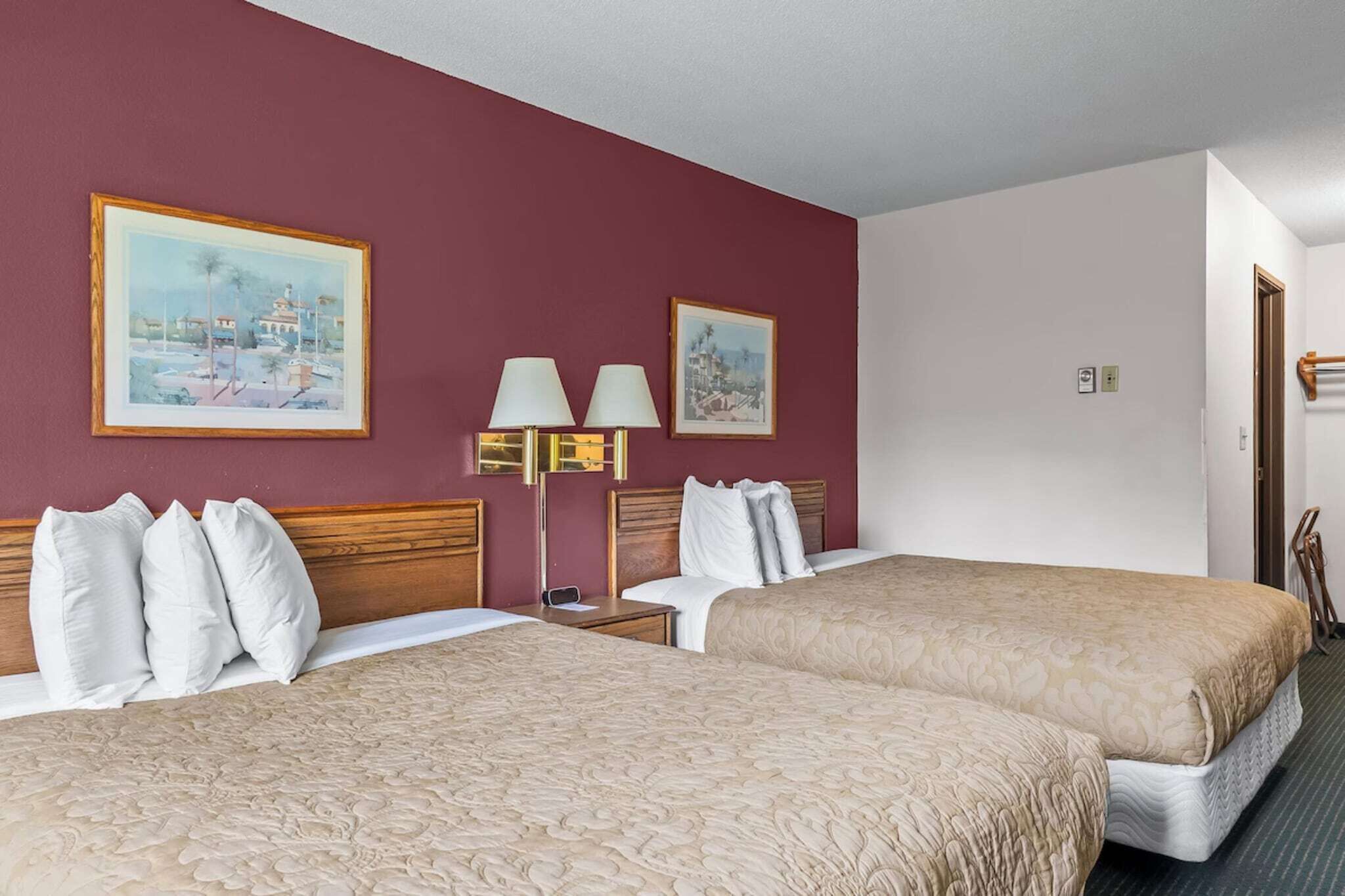 Ein Hotelzimmer mit zwei Betten, einem Nachttisch, einer Lampe und zwei gerahmten Bildern an der Wand.