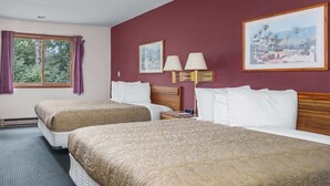 A hotel room with two beds, a window with curtains, a wall-mounted lamp, and a framed picture.