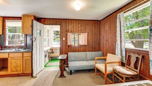 Une pièce aux murs en bois, avec un canapé, un fauteuil, une table et une fenêtre avec des rideaux.