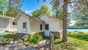 Une cabane blanche avec des fondations en pierre, une véranda en bois et une vue sur le lac.