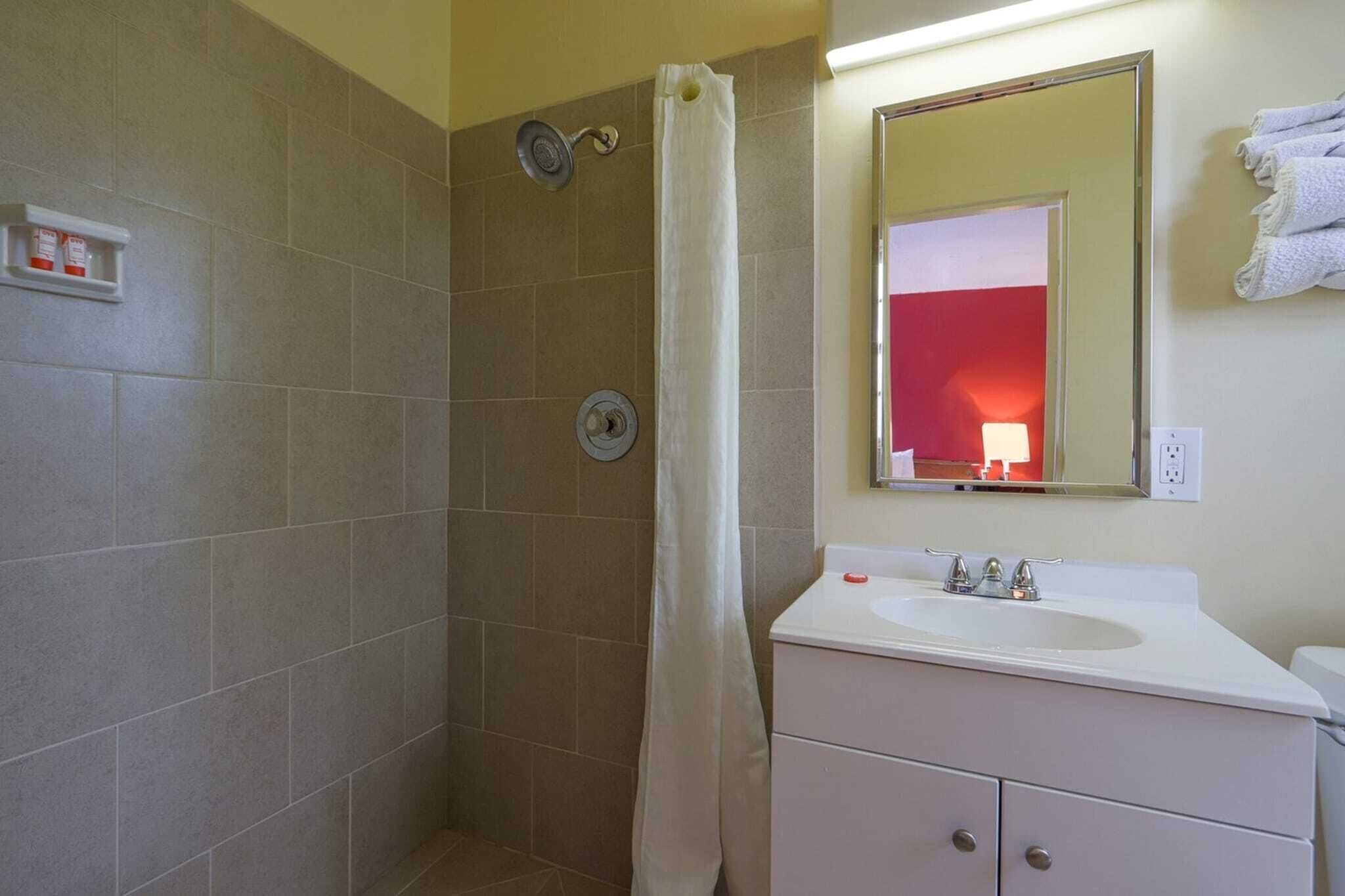 A bathroom with a shower, a sink, a mirror, and a towel rack.
