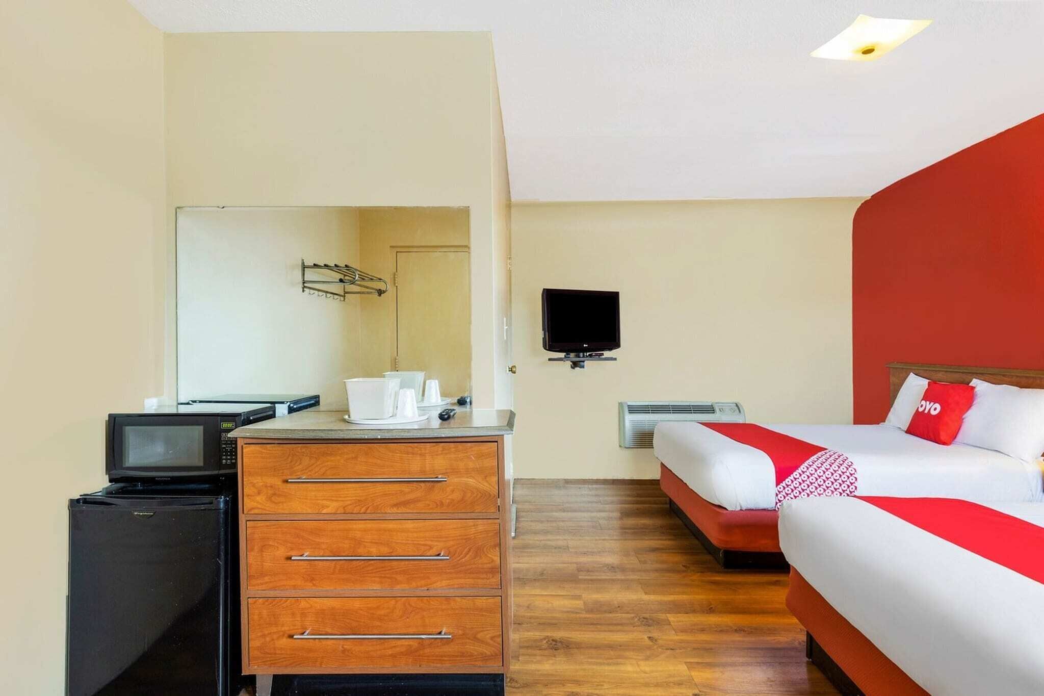 A hotel room with a bed, a TV, a desk with a microwave, and a dresser.