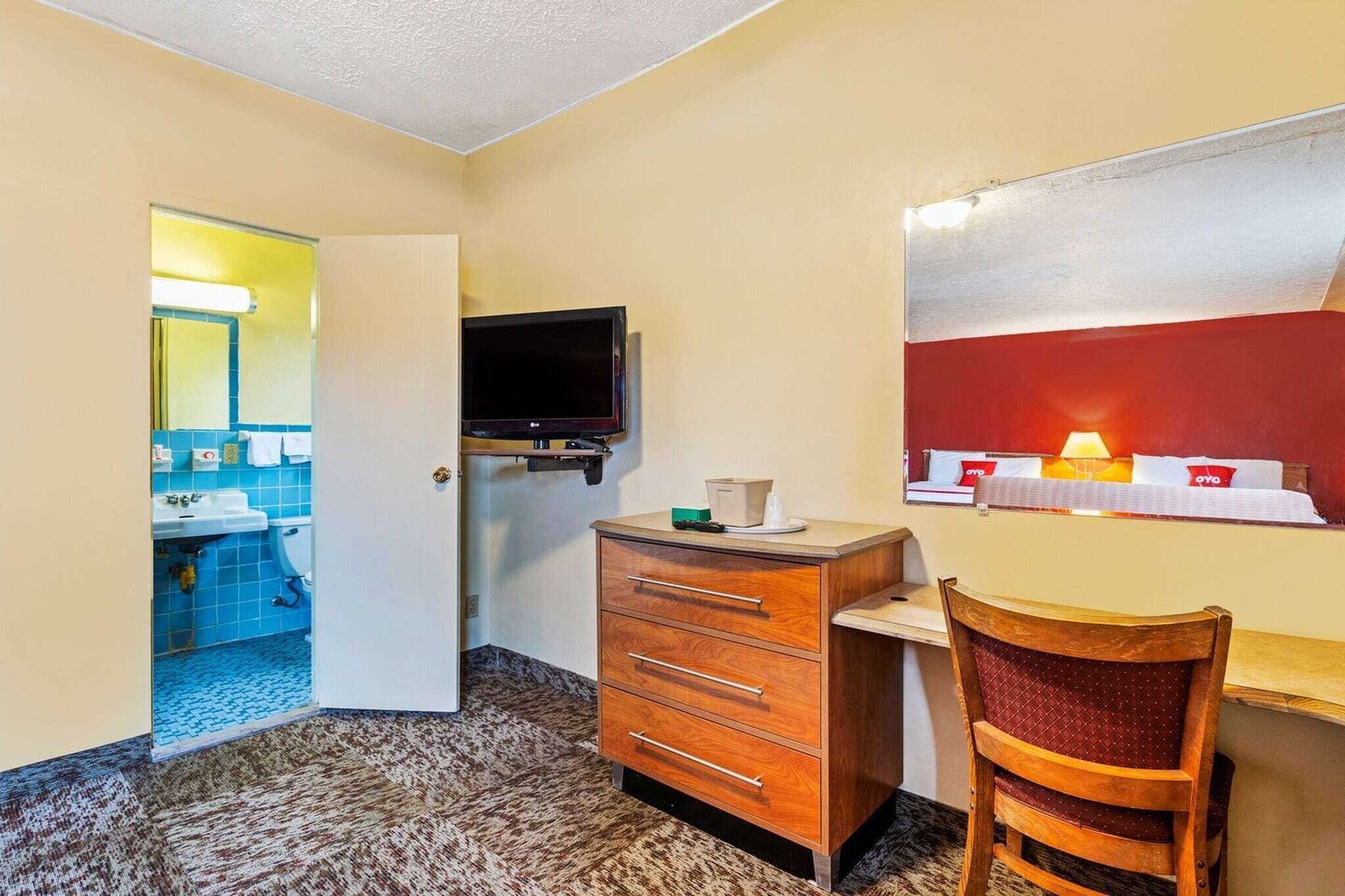 A hotel room with a desk, chair, television, and a view of the hotel lobby.