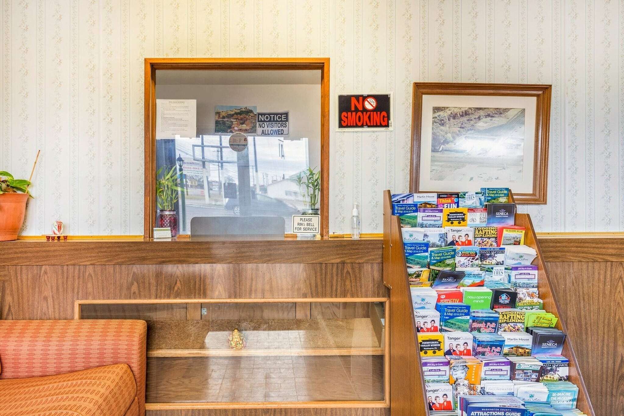 A reception area with a wooden desk, a 'No Smoking' sign, a framed picture, and a display of travel guides.