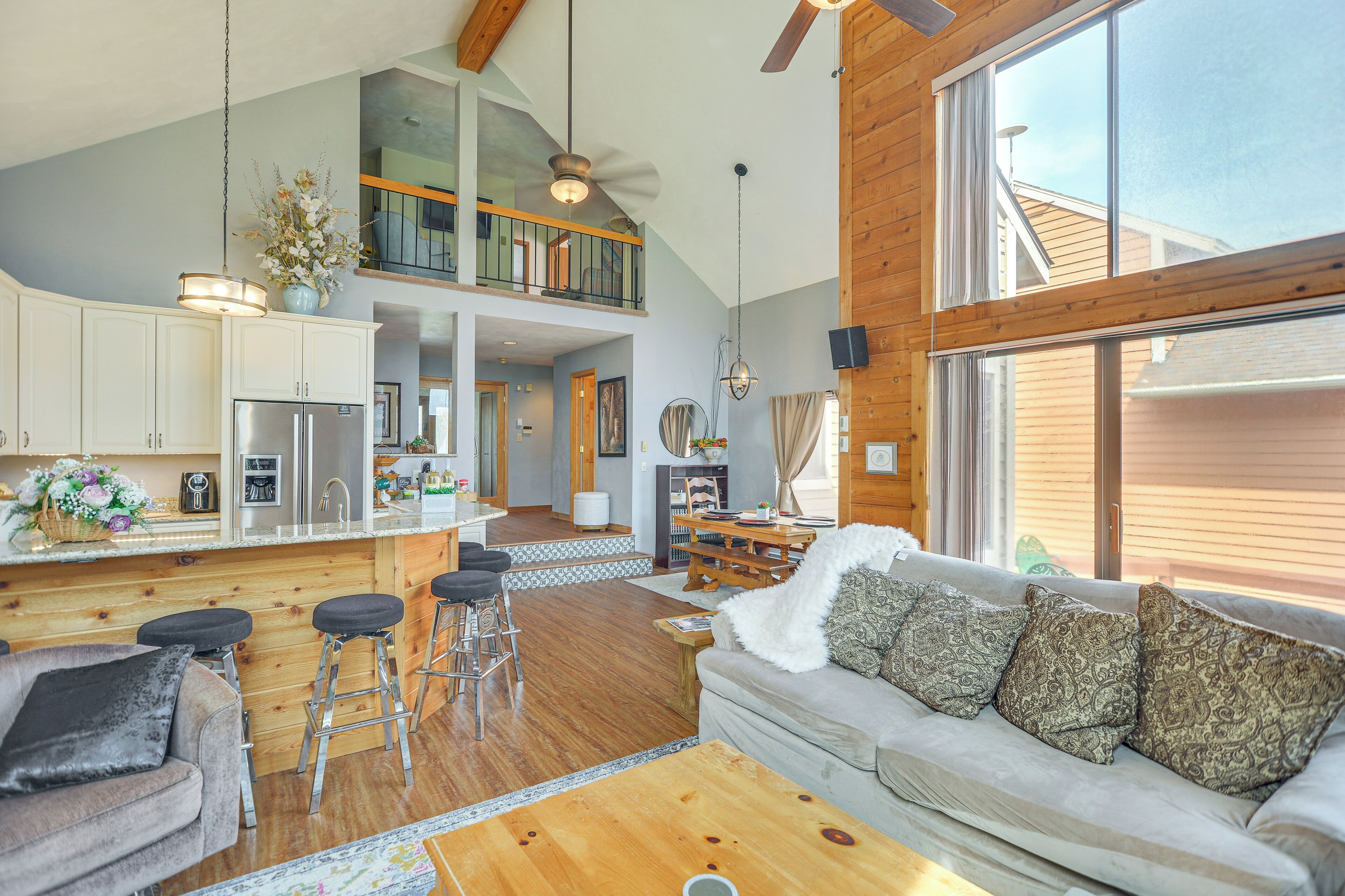 A spacious living area with a high ceiling, a kitchen with a central island, and a cozy seating area with a sofa and bar stools.