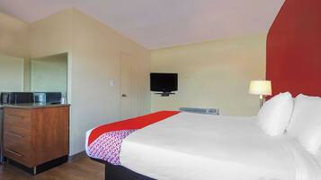 A hotel room with a bed, a desk with a microwave, a TV, and a bedside lamp.