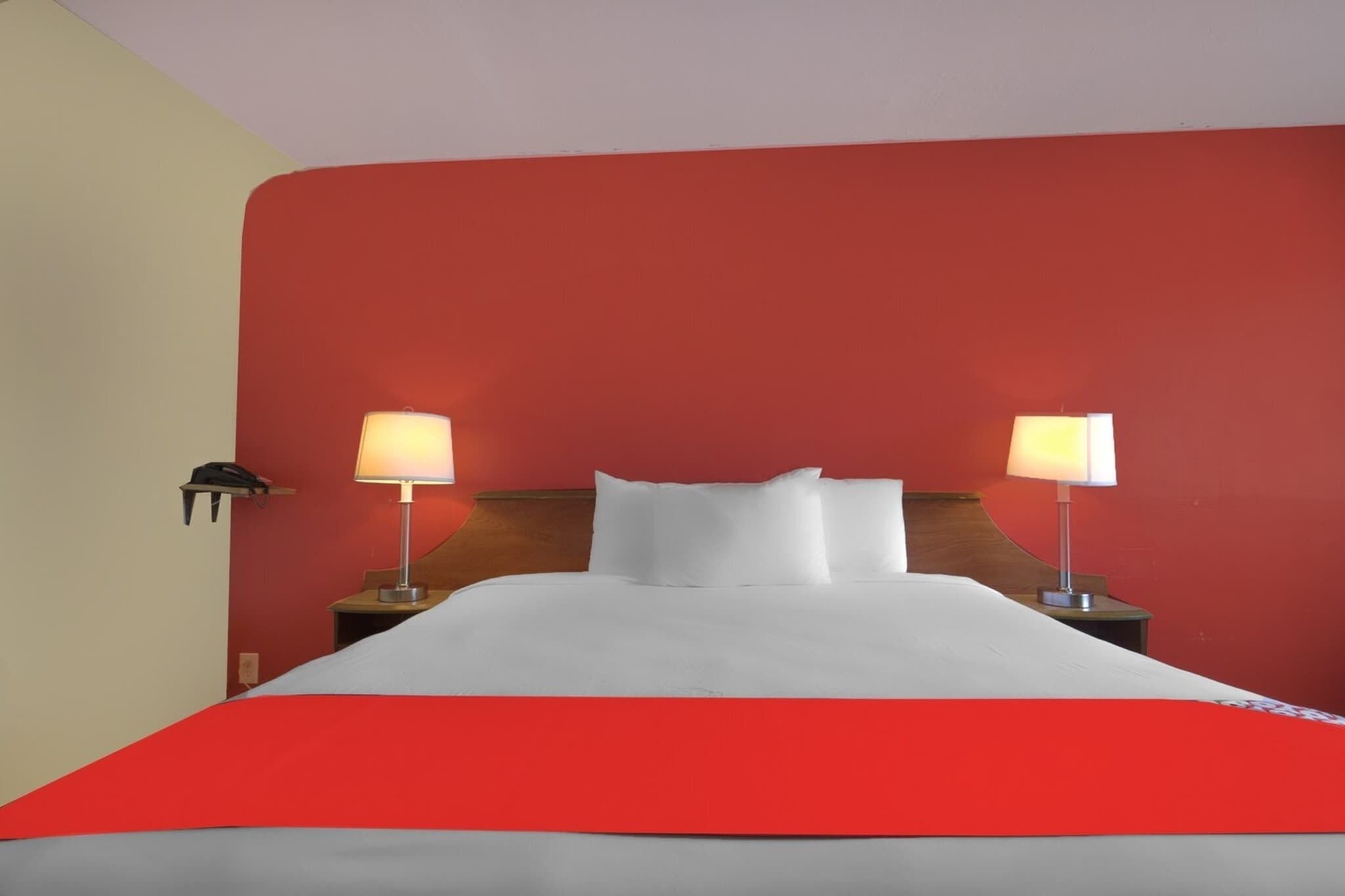 A hotel room with a bed, two bedside lamps, and a red wall.