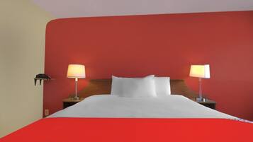 A hotel room with a bed, two bedside lamps, and a red wall.